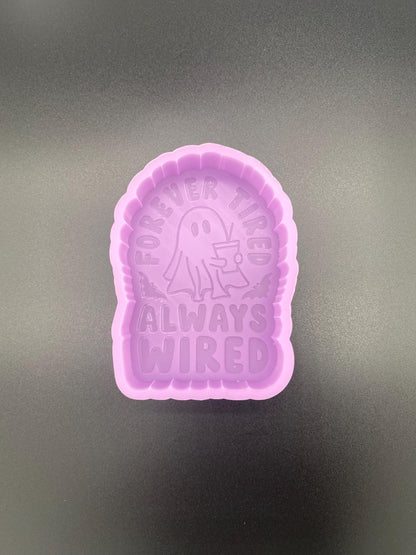 May include: A purple silicone mold with a ghost holding a cup and the text &#39;Forever Tired Always Wired&#39;.